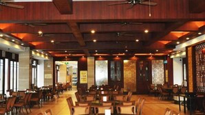 A spacious restaurant with wooden ceiling beams, multiple ceiling fans, and a variety of seating arrangements including round tables and chairs. - Daxiagu Ligong Guoyuan Holiday Hotel (Ruyuan)