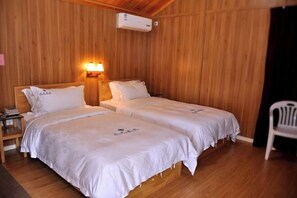 A room with two beds, wooden walls, a nightstand, a chair, and an air conditioning unit. - Daxiagu Ligong Guoyuan Holiday Hotel (Ruyuan)
