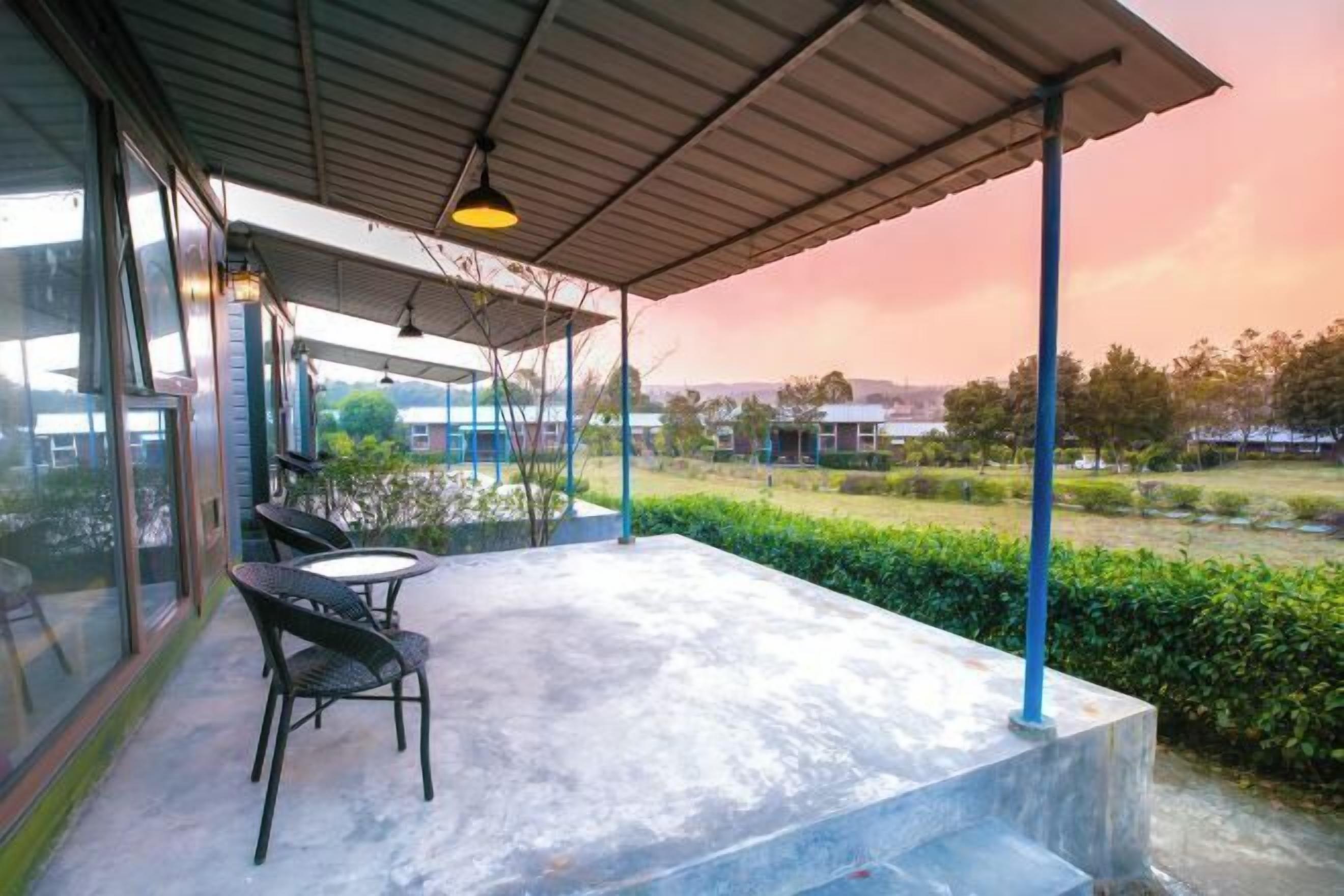 Un espacio cubierto al aire libre con una mesa y sillas, con vistas a un jardín ajardinado y edificios lejanos.