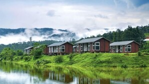 A row of red houses by a calm lake with a forested mountain backdrop. - Daxiagu Ligong Guoyuan Holiday Hotel (Ruyuan)
