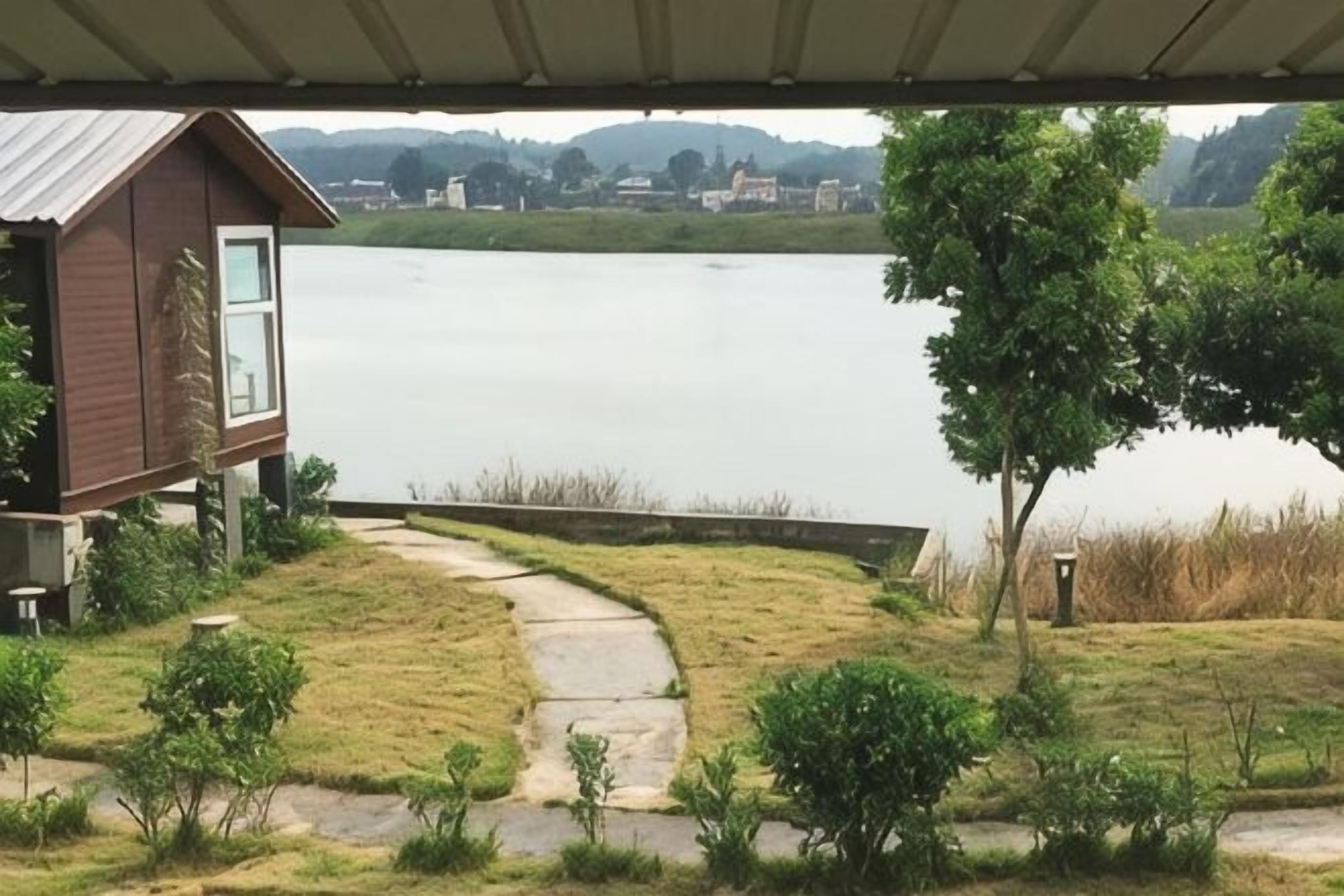 A lakeside property with a wooden cabin, a stone pathway, and a grassy area with small bushes.
