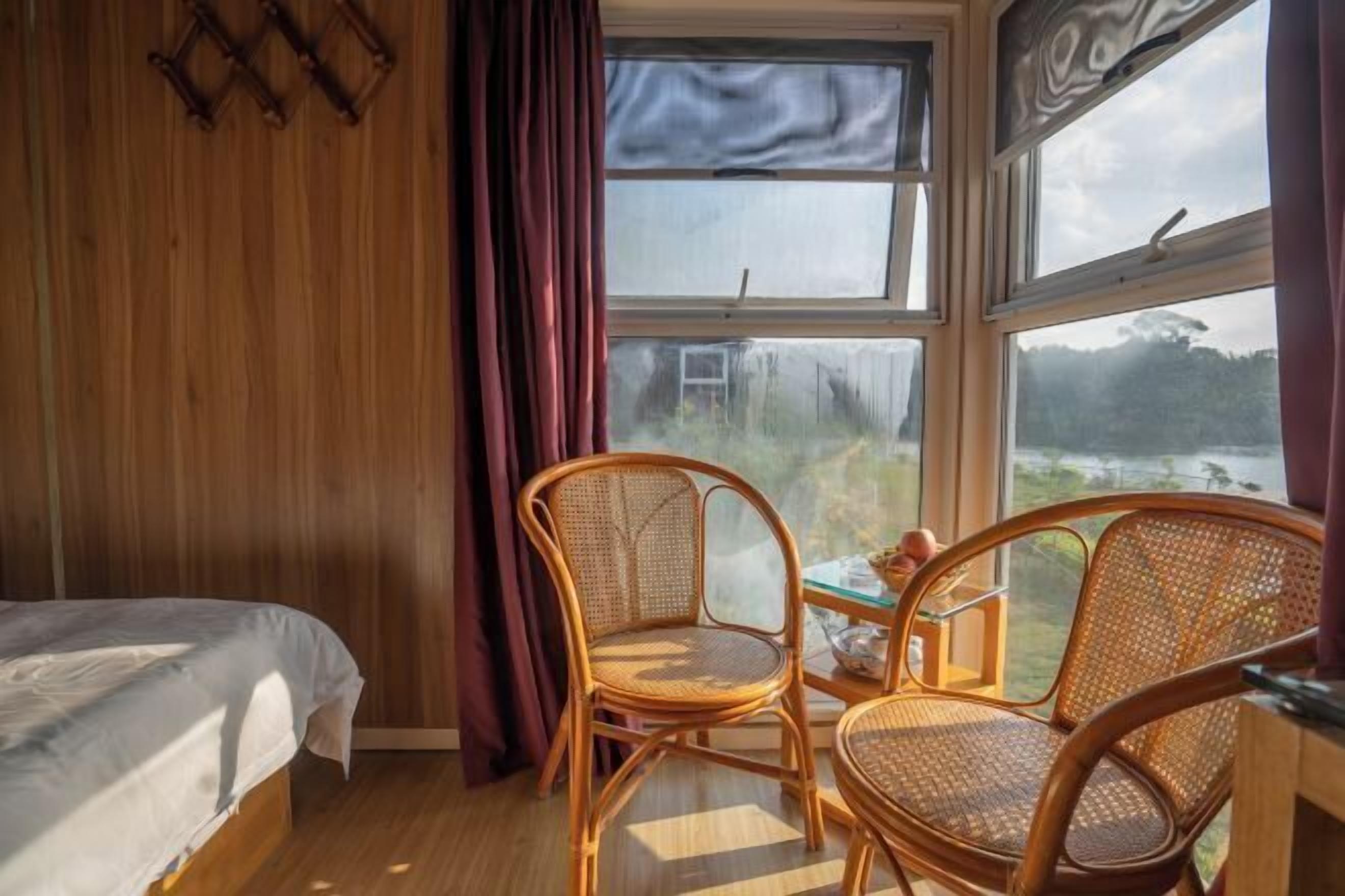 Una habitación con una cama, dos sillas de mimbre, una mesa y un ventanal que ofrece vistas al exterior.