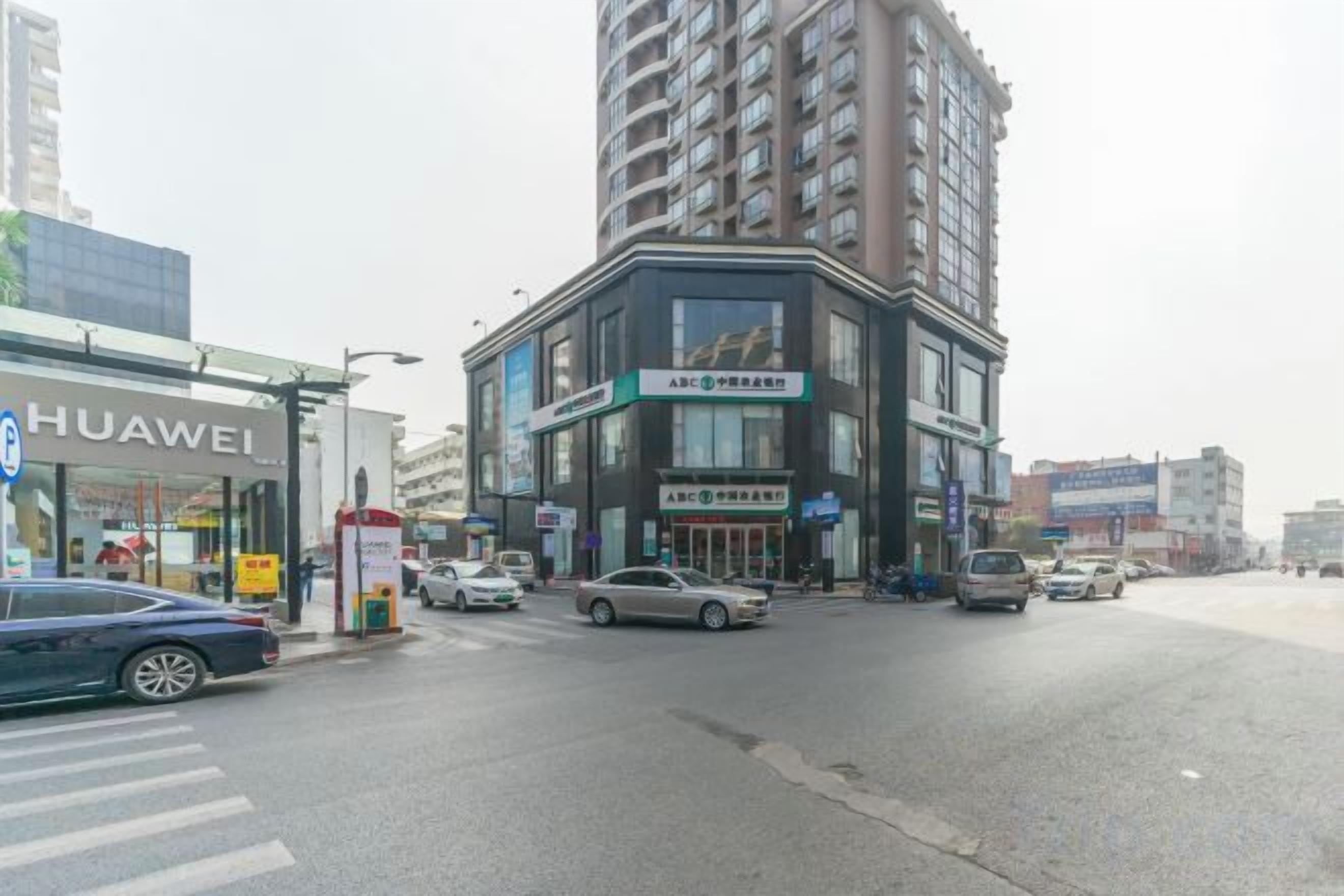 A street view with a Huawei store, a multi-story building with signage, and several cars.