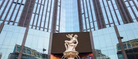 A modern building with a reflective glass facade and a central fountain sculpture.