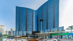 A modern building with a glass facade, a clock, and storefronts including Huawei and Oppo. - Sibaike Hotel (Zhongshan)