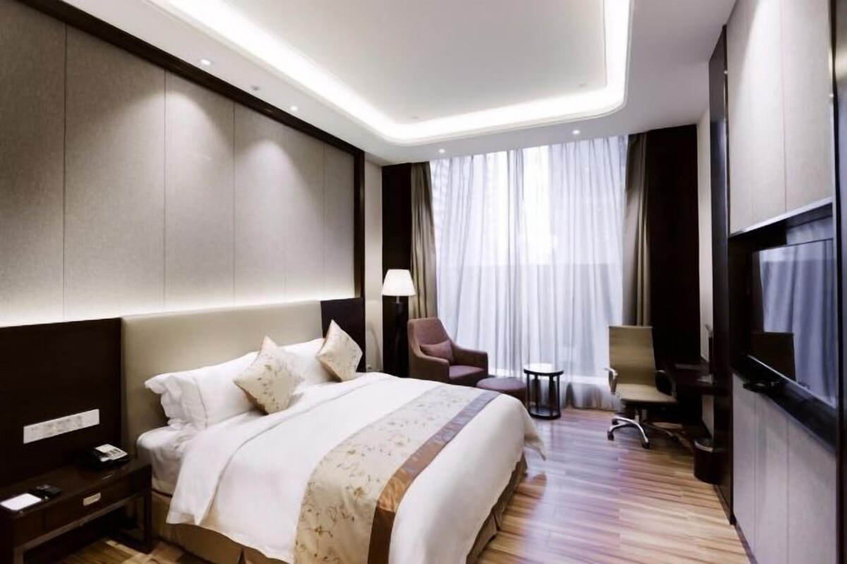 Habitación de hotel con una cama grande, un escritorio, una silla, un televisor y una ventana con cortinas.