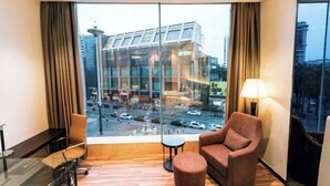 A hotel room with a large window, a sofa, a chair, a small table, and a lamp. - Sibaike Hotel (Zhongshan)