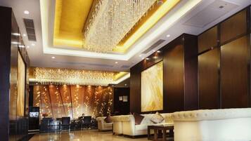 A hotel lobby with a reception desk, seating area, and a large chandelier.