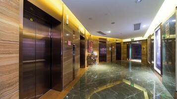 A modern hotel lobby with marble flooring, wooden paneling, and a central elevator.