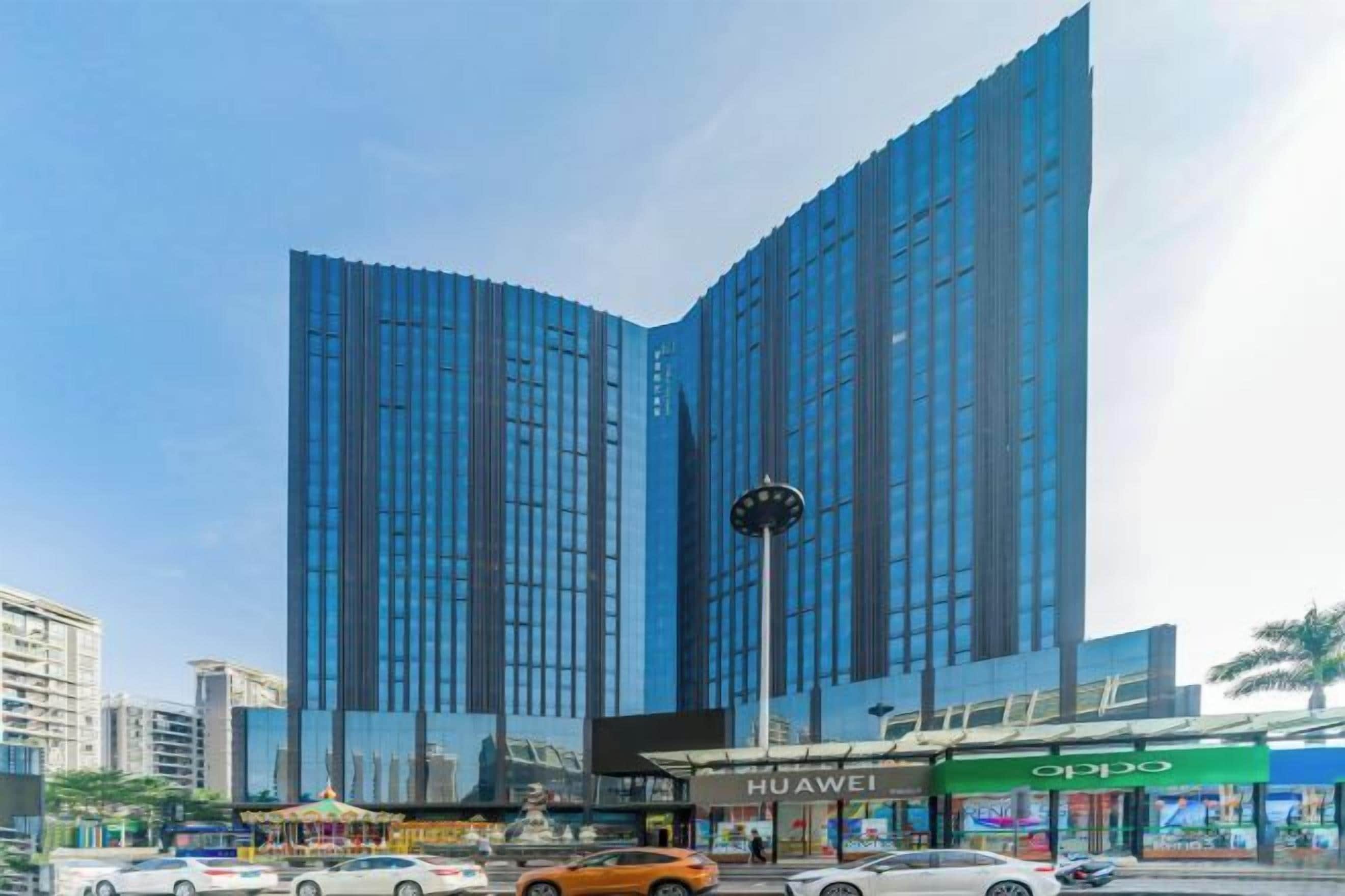 A modern high-rise building with reflective glass windows, a prominent clock, and commercial establishments at the base.
