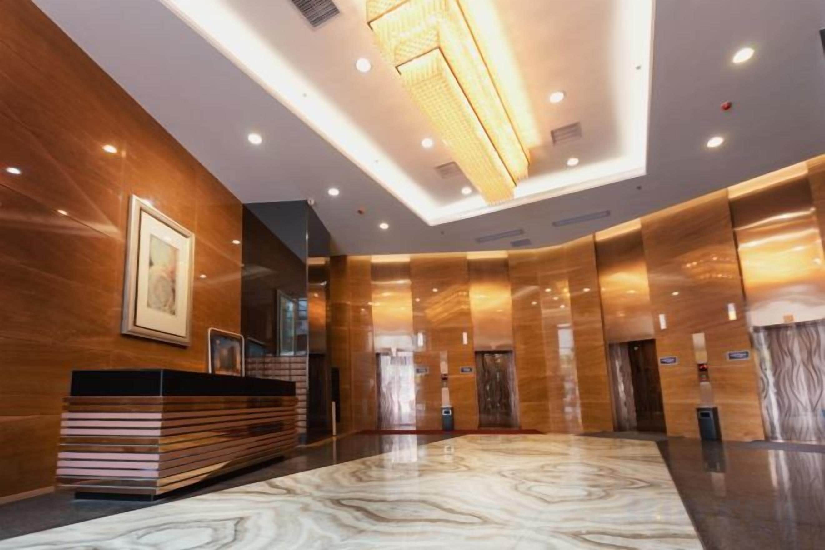A modern hotel lobby with a reception desk, elevators, and a marble floor.