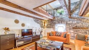 A living room with a stone wall, wooden beams, a sofa, a coffee table, and a TV. - Countryside House Gal (Sezana)