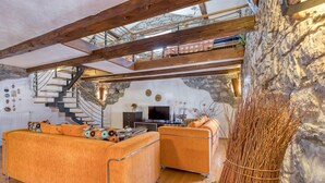 A modern living room with a stone wall, wooden beams, a staircase, and a fireplace. - Countryside House Gal (Sezana)