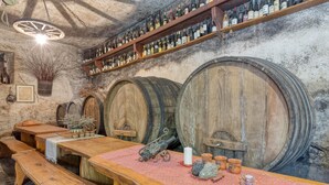A rustic cellar with wooden barrels, a long wooden table, benches, and shelves of wine bottles. - Countryside House Gal (Sezana)