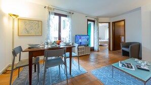 Ein Essbereich mit Tisch für vier Personen, einem Fernseher und einer Sitzecke mit Sofa und Sesseln.