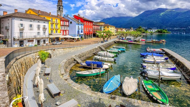 Eine Uferpromenade mit bunten Gebäuden, einer Steinmauer und Booten, die am Wasser liegen.