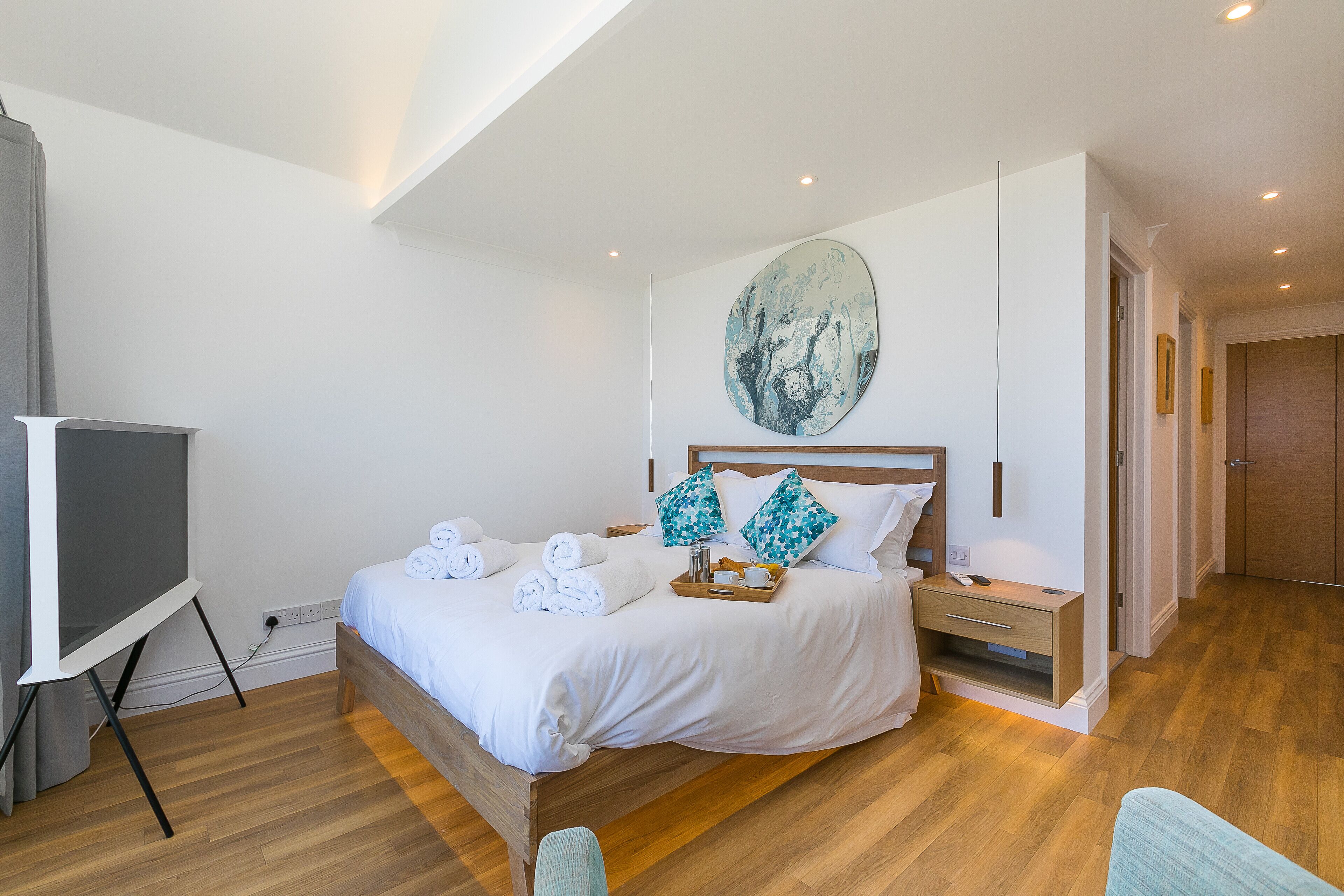A bedroom with a bed, a bedside table, a wall-mounted artwork, and a wooden floor.