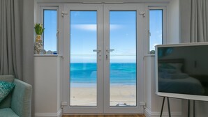 Une pièce dotée d’une grande porte-fenêtre coulissante donnant sur la plage, d’un tableau blanc sur pied et d’un fauteuil turquoise.