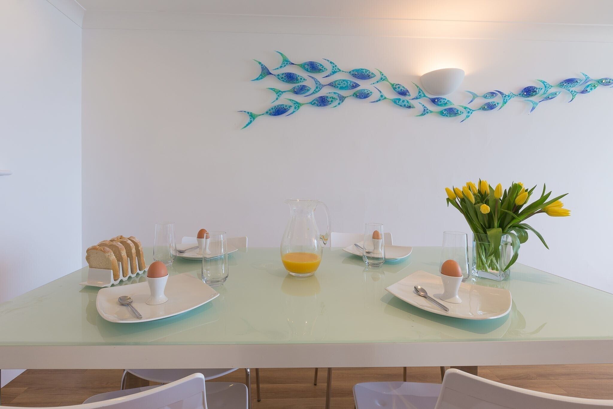 A breakfast table set with plates, toast, eggs, a pitcher of orange juice, and a vase of yellow flowers.