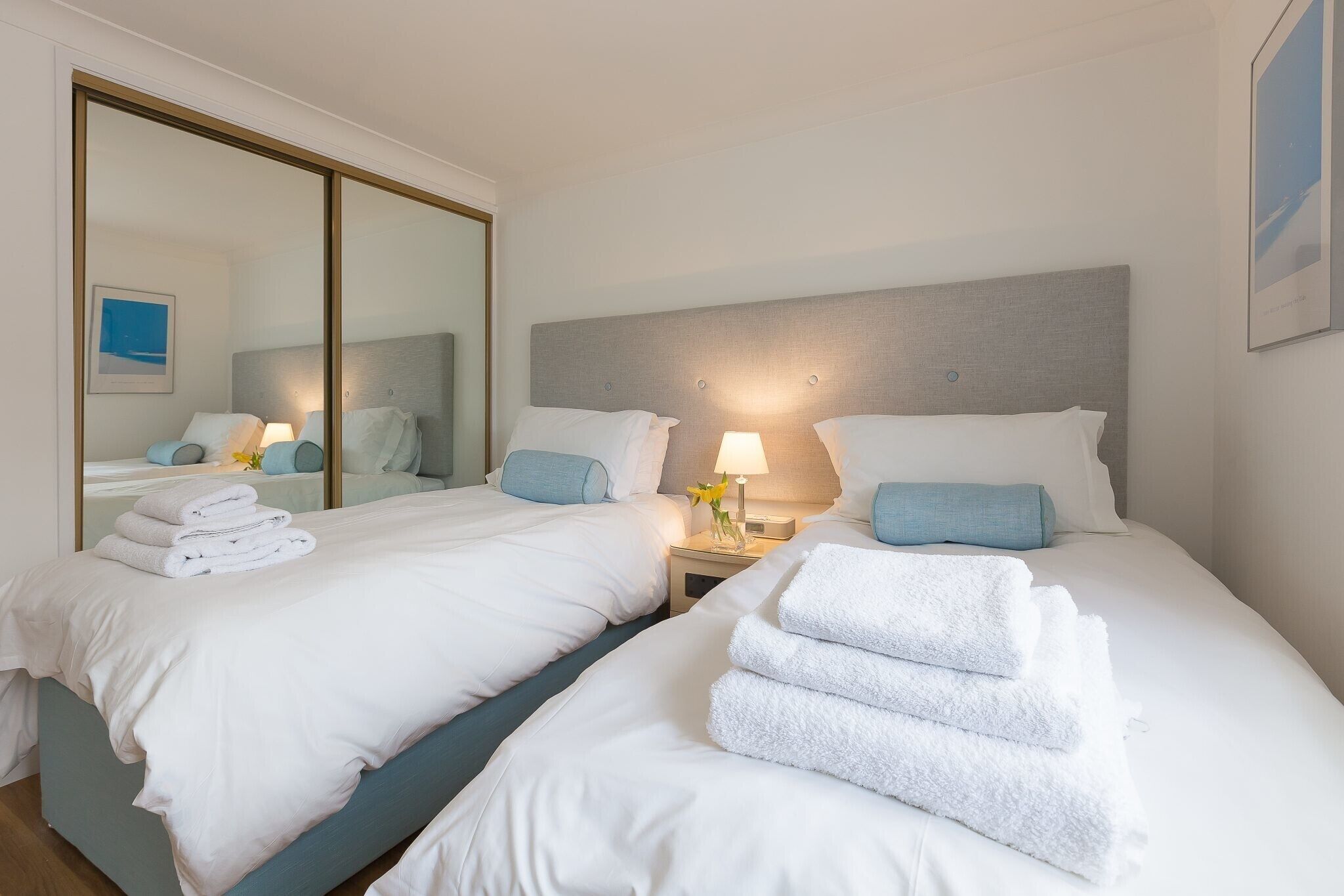 A hotel room with two beds, white linens, a large mirror, and a nightstand with a lamp.