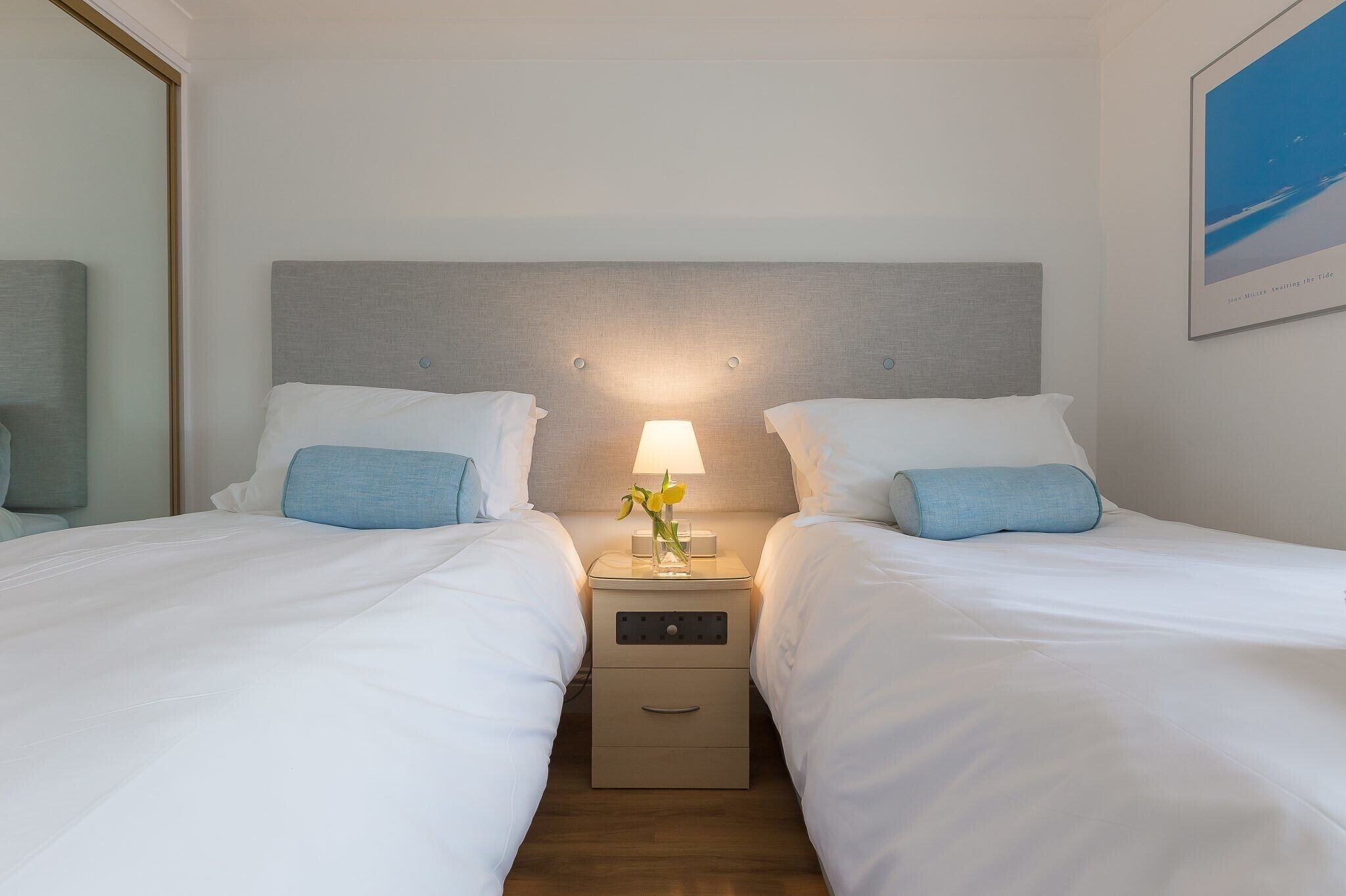 Ein Hotelzimmer mit zwei Betten, einem Nachttisch mit Lampe und einem gerahmten Bild an der Wand.