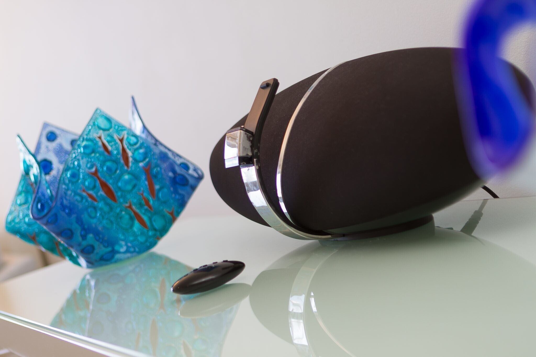 A glass table with a decorative blue glass object and a black object on it.