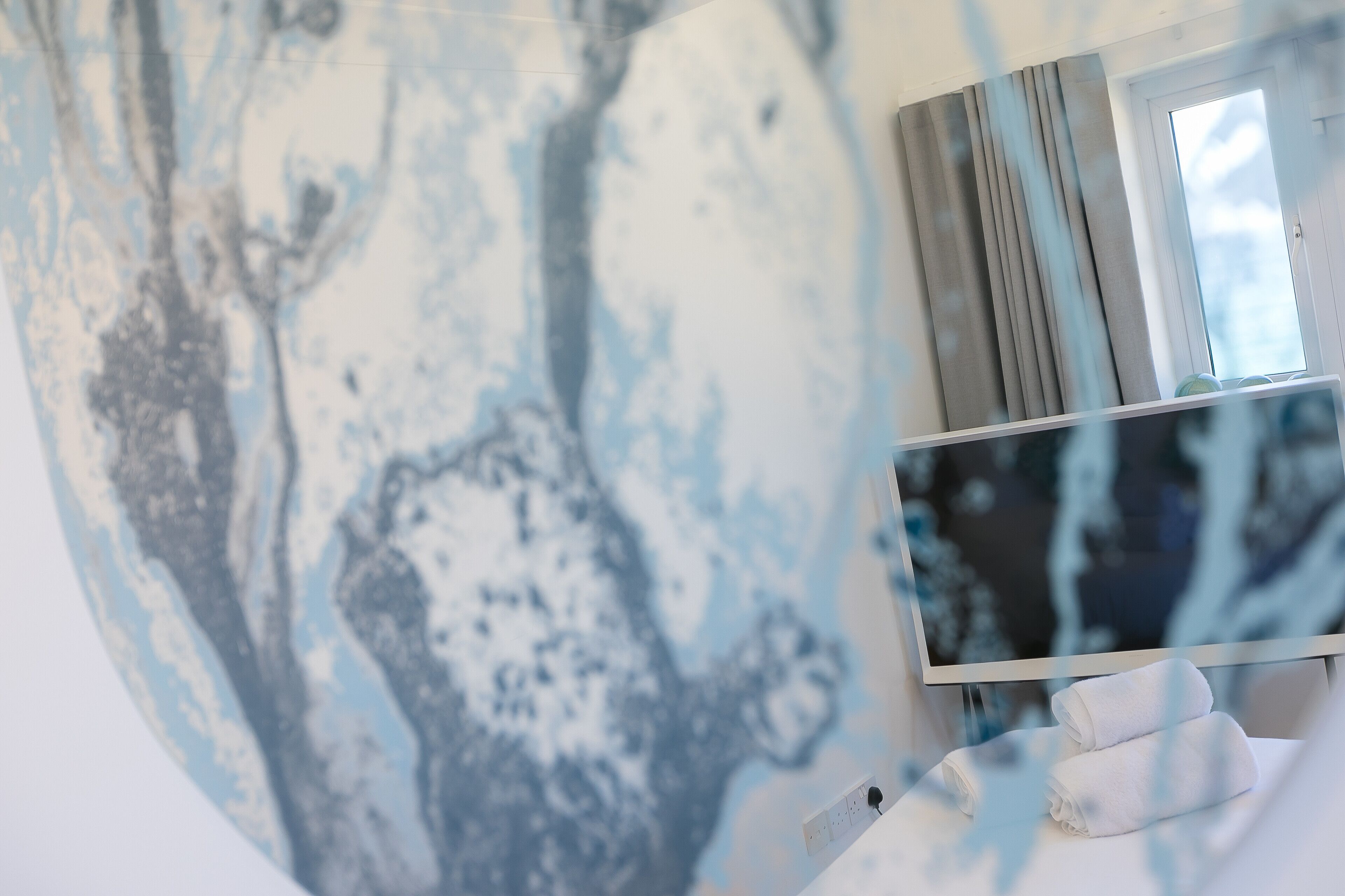 Una habitación con un ventanal grande, un televisor de pantalla plana y una pared con un mural texturizado.