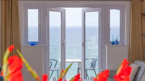 Une pièce dotée d’une grande porte vitrée donnant sur un balcon avec vue sur la mer. On y trouve une petite table et des chaises.