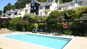 Ein Swimmingpool mit einer Pergola und Liegestühlen, umgeben von üppiger Bepflanzung und mehrstöckigen Wohngebäuden.