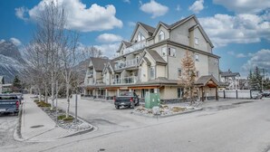 A multi-story hotel with a balcony on the second floor, a parking lot, and a mountain backdrop. - Spacious Condo, Great Location & Mountain Views (Canmore)
