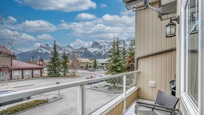 A balcony with a view of a snowy mountain range, a parking lot, and a building with a red roof. - Spacious Condo, Great Location & Mountain Views (Canmore)
