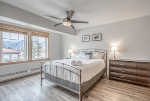A bedroom with a bed, a ceiling fan, a dresser, and a window with a view of mountains.