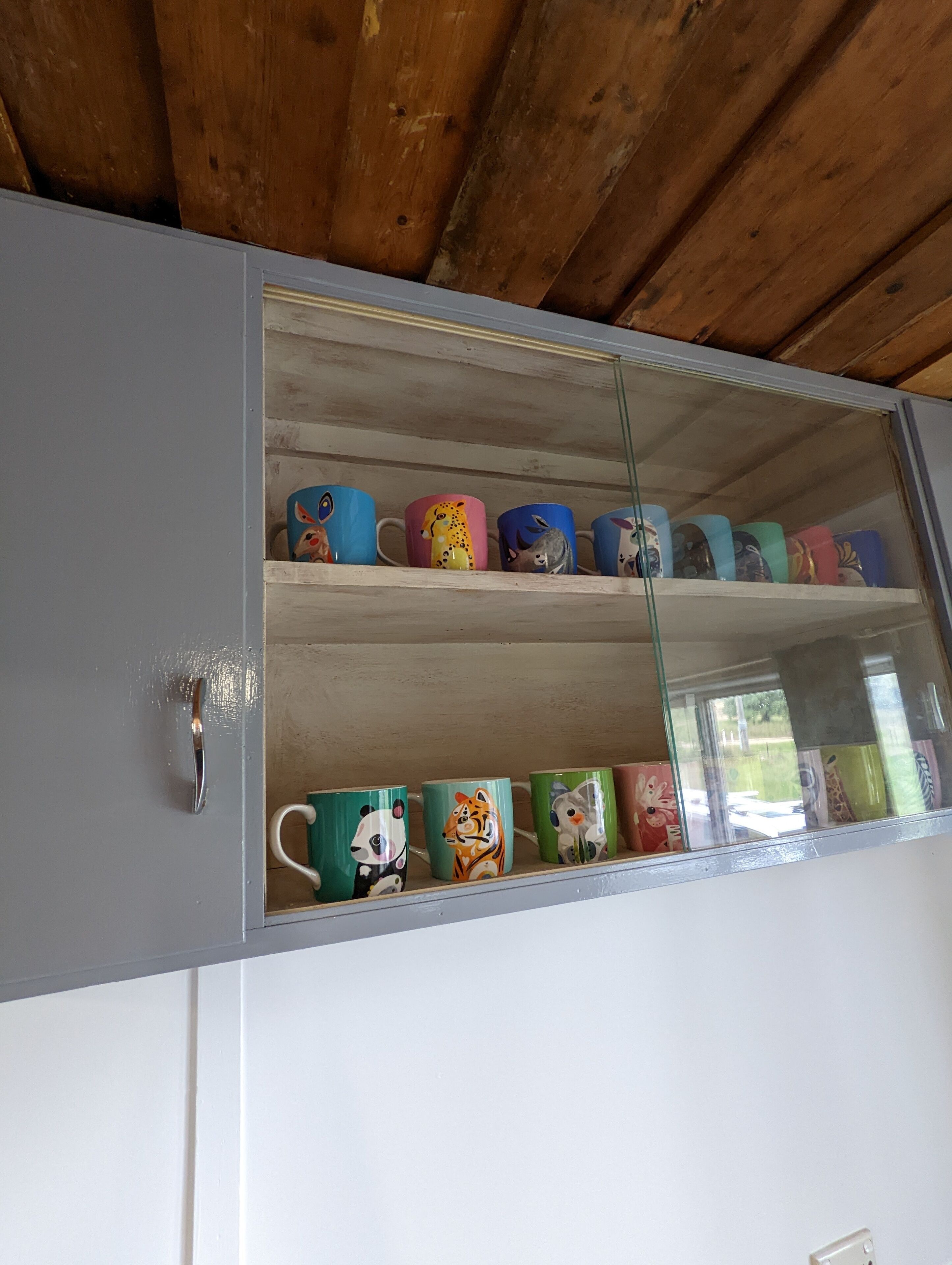A cabinet with a glass door displaying mugs with animal designs.