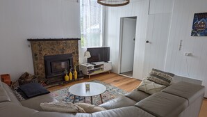 Un salon avec une cheminée en pierre, un canapé blanc, une table basse et un téléviseur posé sur un meuble blanc.