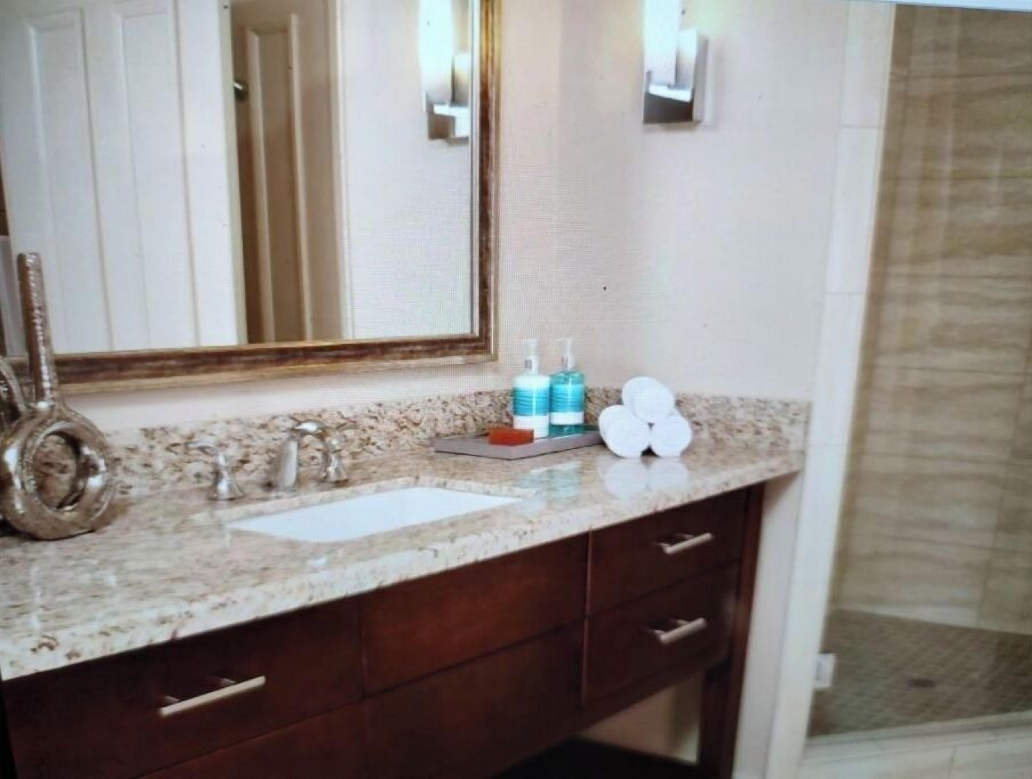 A bathroom with a marble countertop, a sink, a mirror, and toiletries.