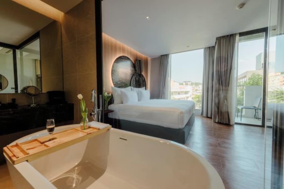 A modern hotel room with a large bed, a bathtub, and a view of the city.