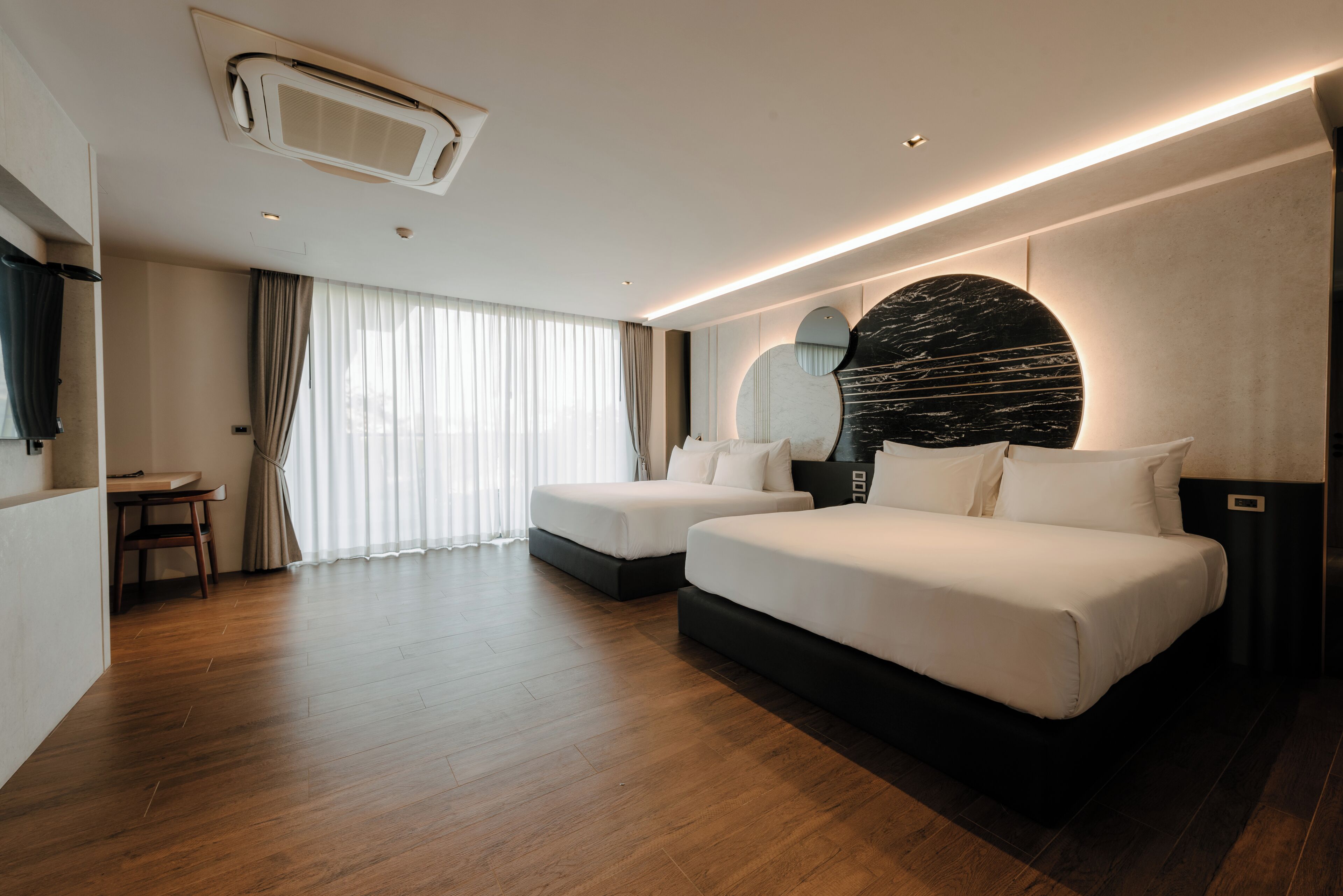A modern hotel room with two beds, a dining area, and a large mirror.