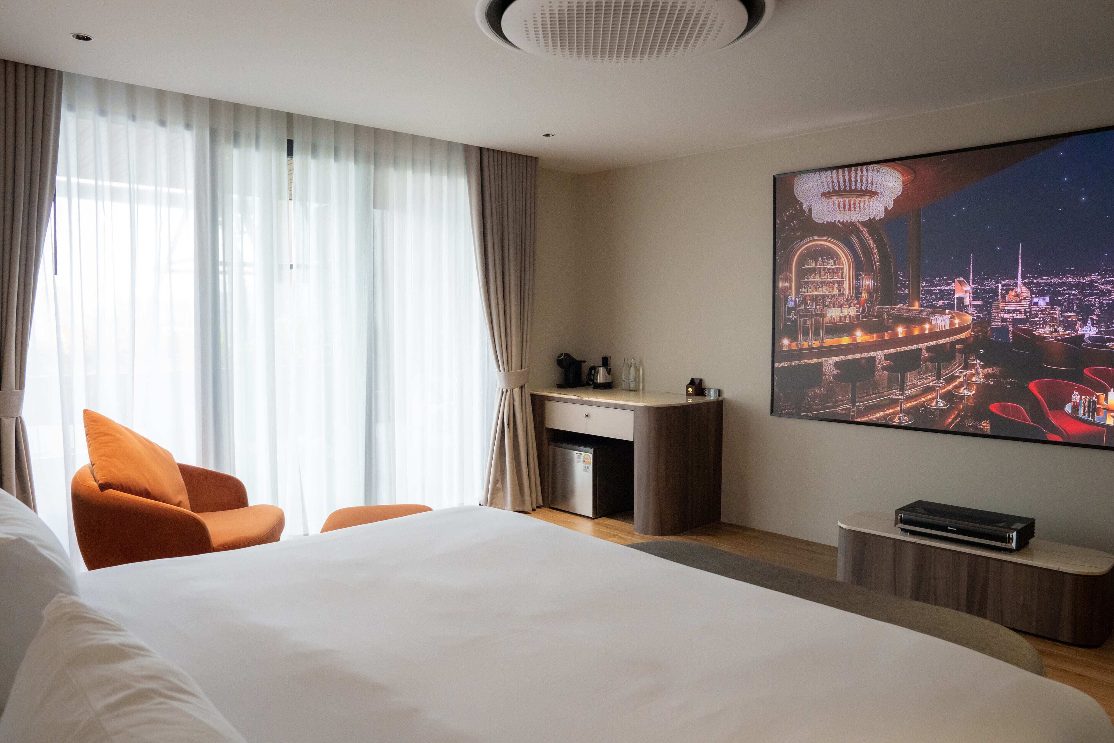 A hotel room with a large bed, a desk, a chair, a TV, and a cityscape view.