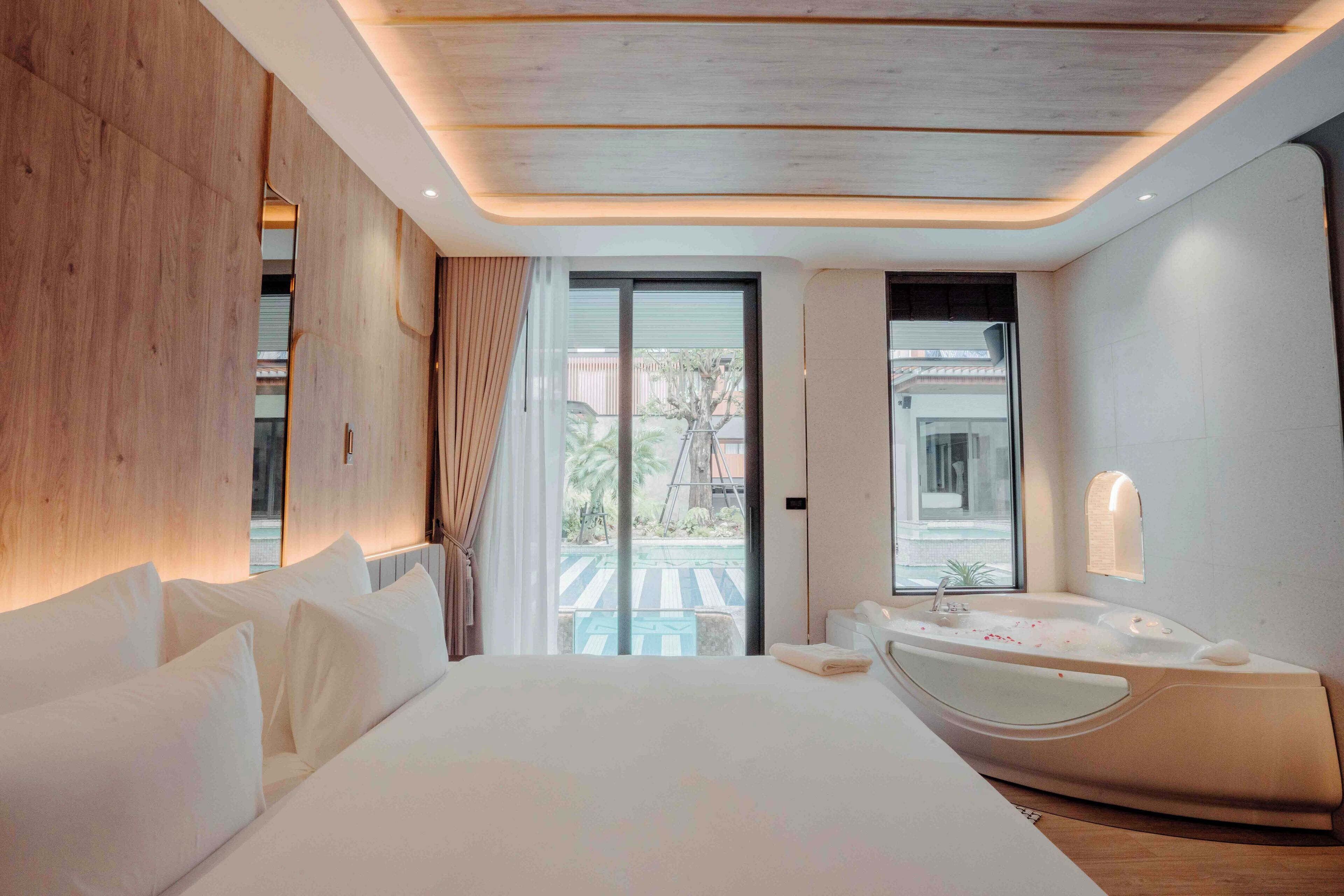 A modern hotel room with a large bed, a bathtub, and a balcony with a view of palm trees.