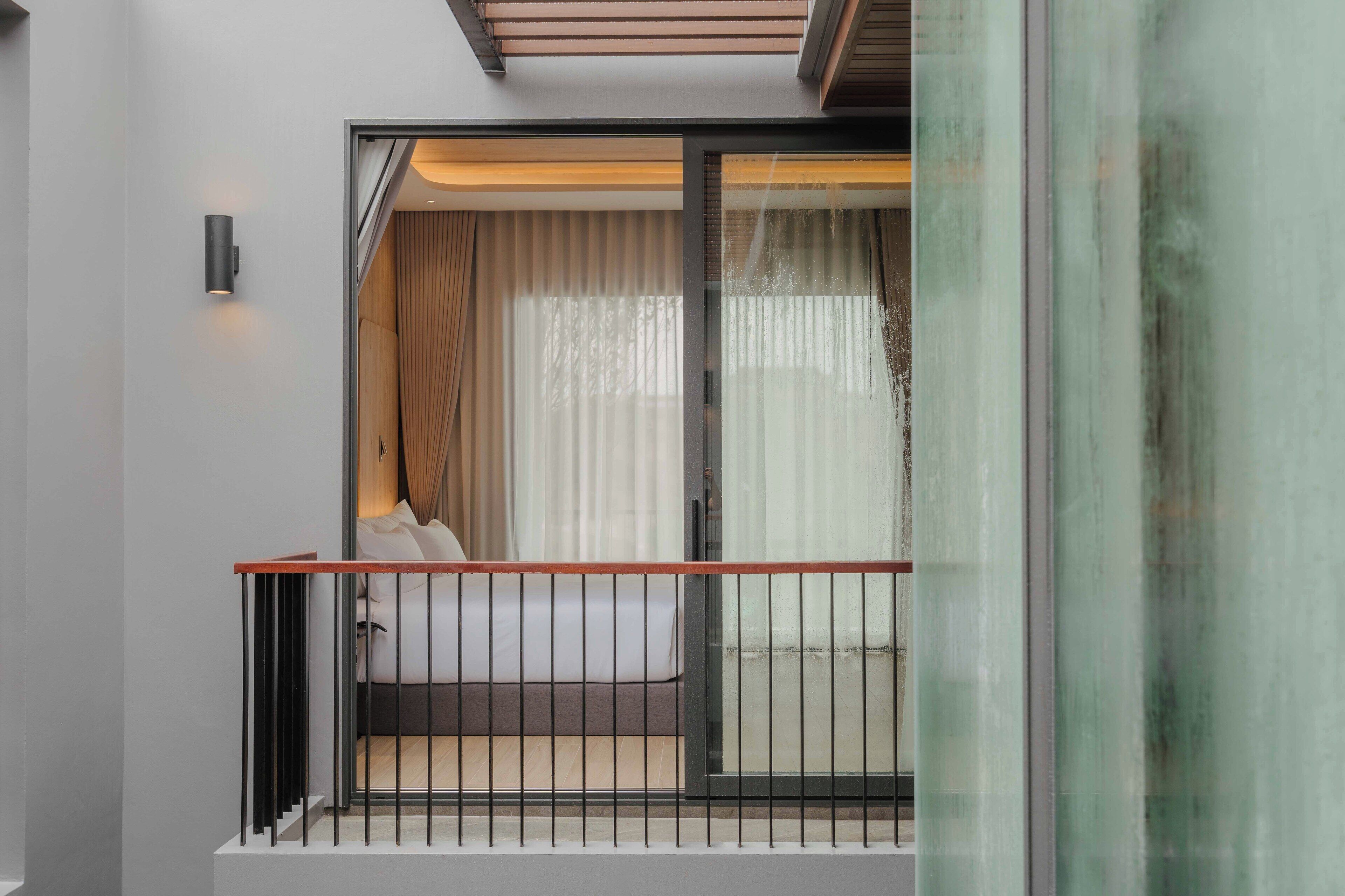 A modern bedroom with a large sliding glass door, a bed with white linens, and a wooden floor.