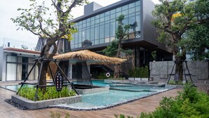 A modern hotel with a swimming pool, a thatched-roof structure, and a stone wall.