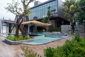A modern hotel with a swimming pool, a thatched-roof structure, and a stone wall.