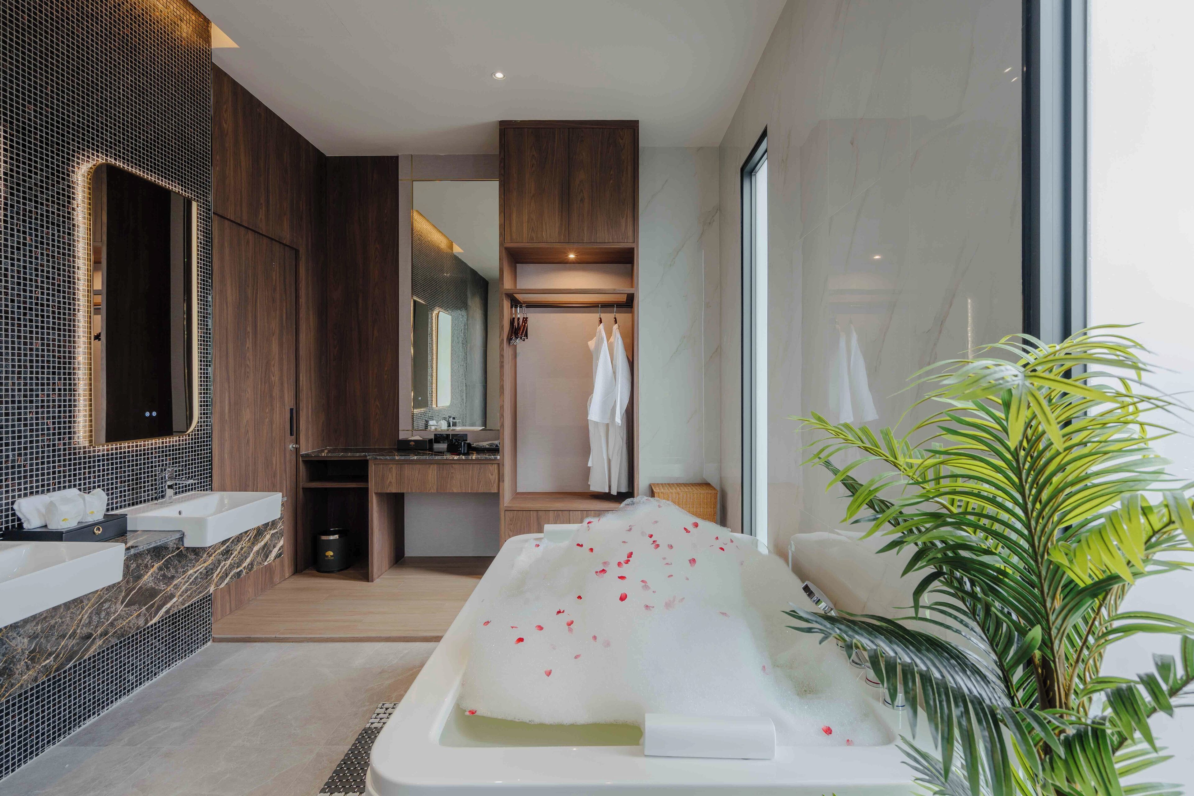 A modern bathroom with a large bathtub, a mirror, and a plant.