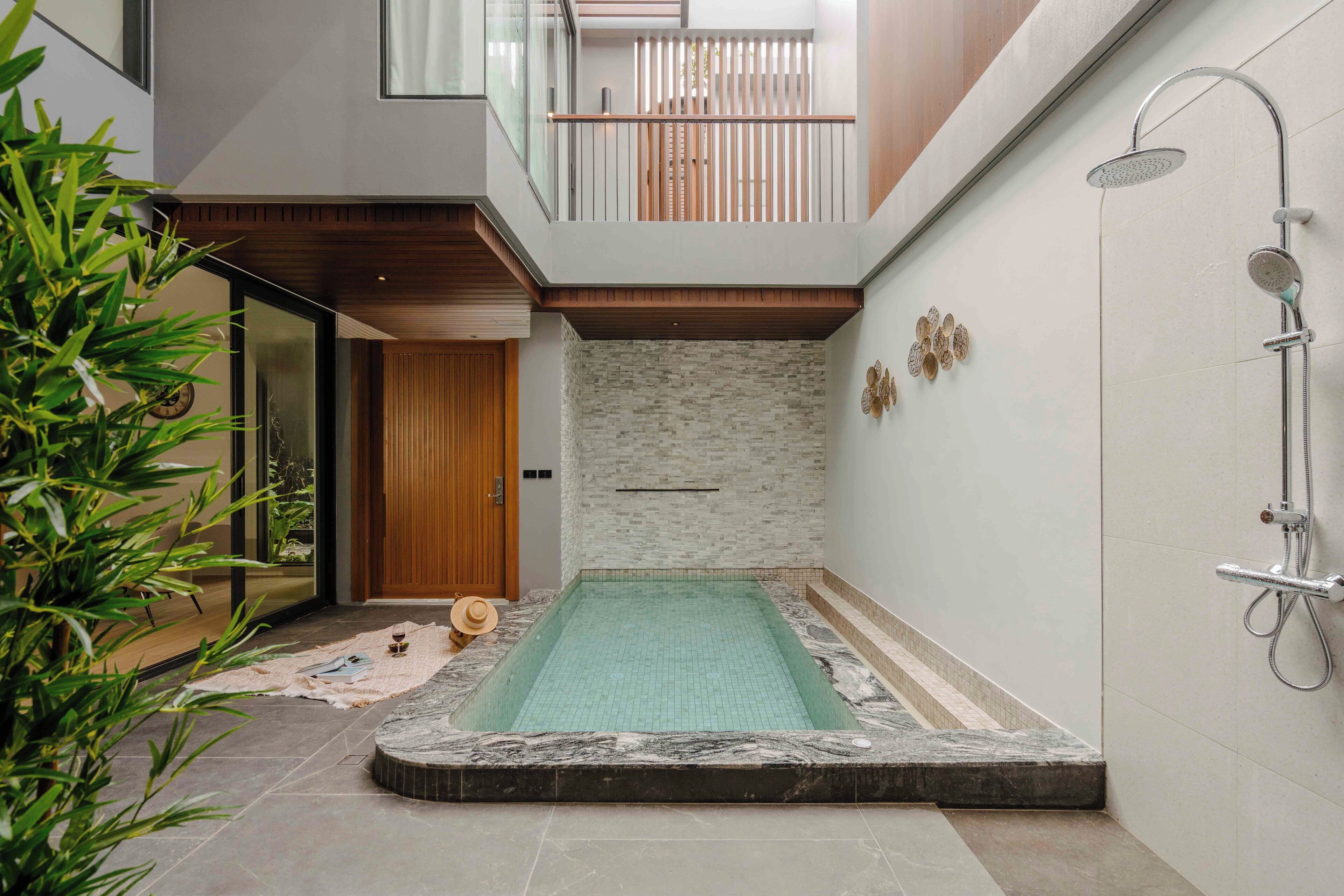 Uma área interna de piscina moderna com uma porta de madeira, um pequeno espaço de estar e um chuveiro.