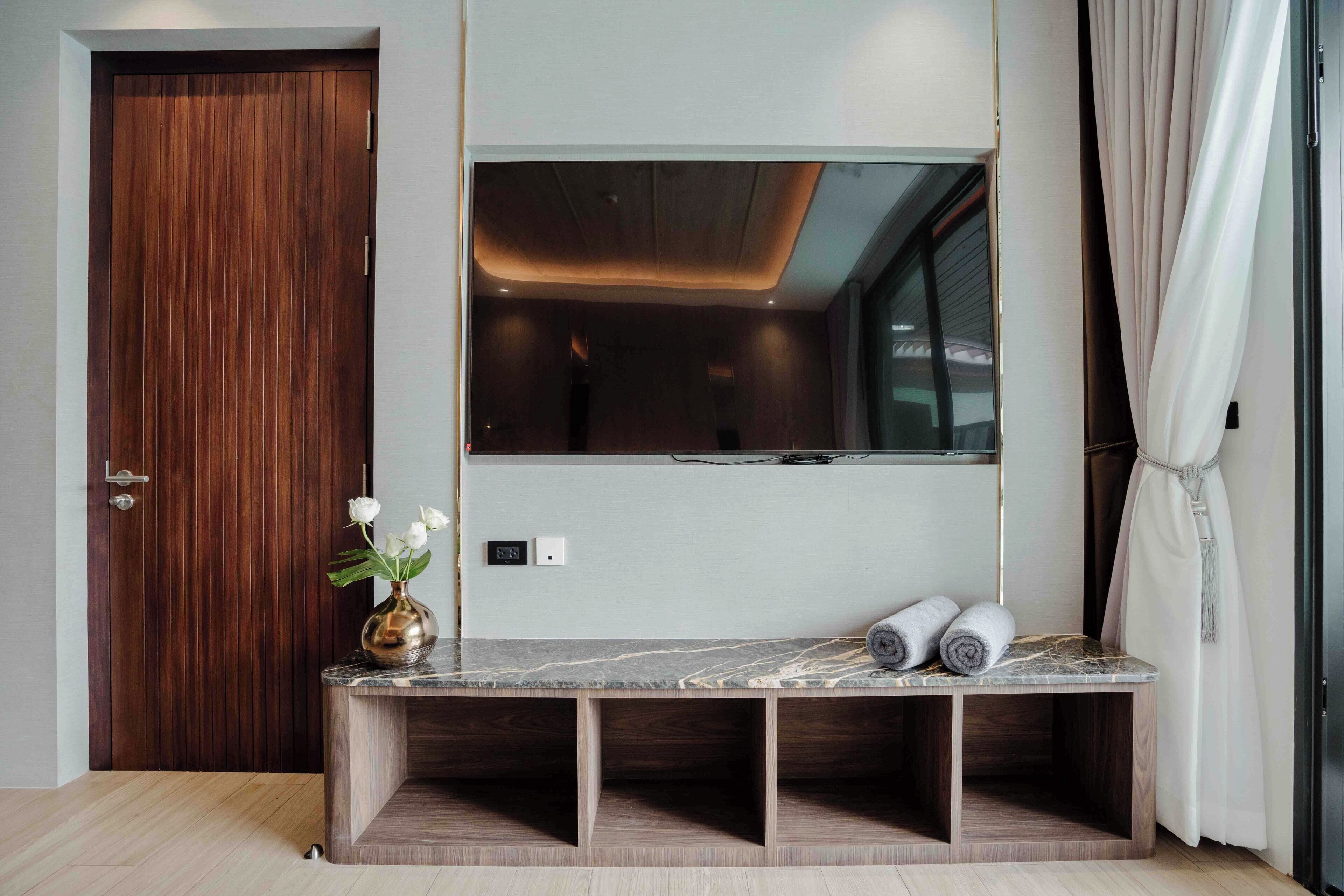 Un baño moderno con puerta de madera, un espejo grande, tocador de mármol y una pequeña zona de estar.