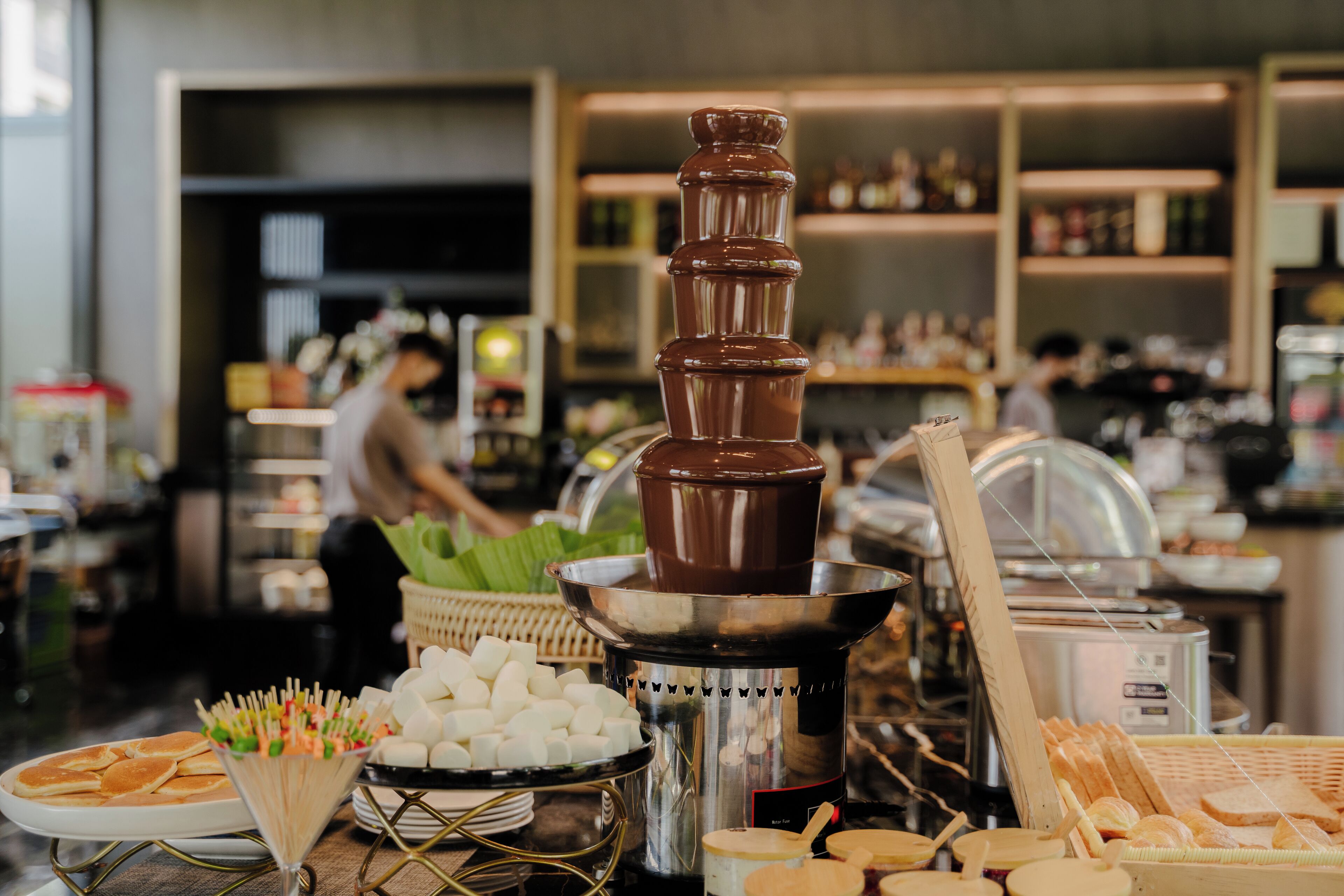 Montaje de bufé con una fuente de chocolate, diversos alimentos y una barra de servicio.