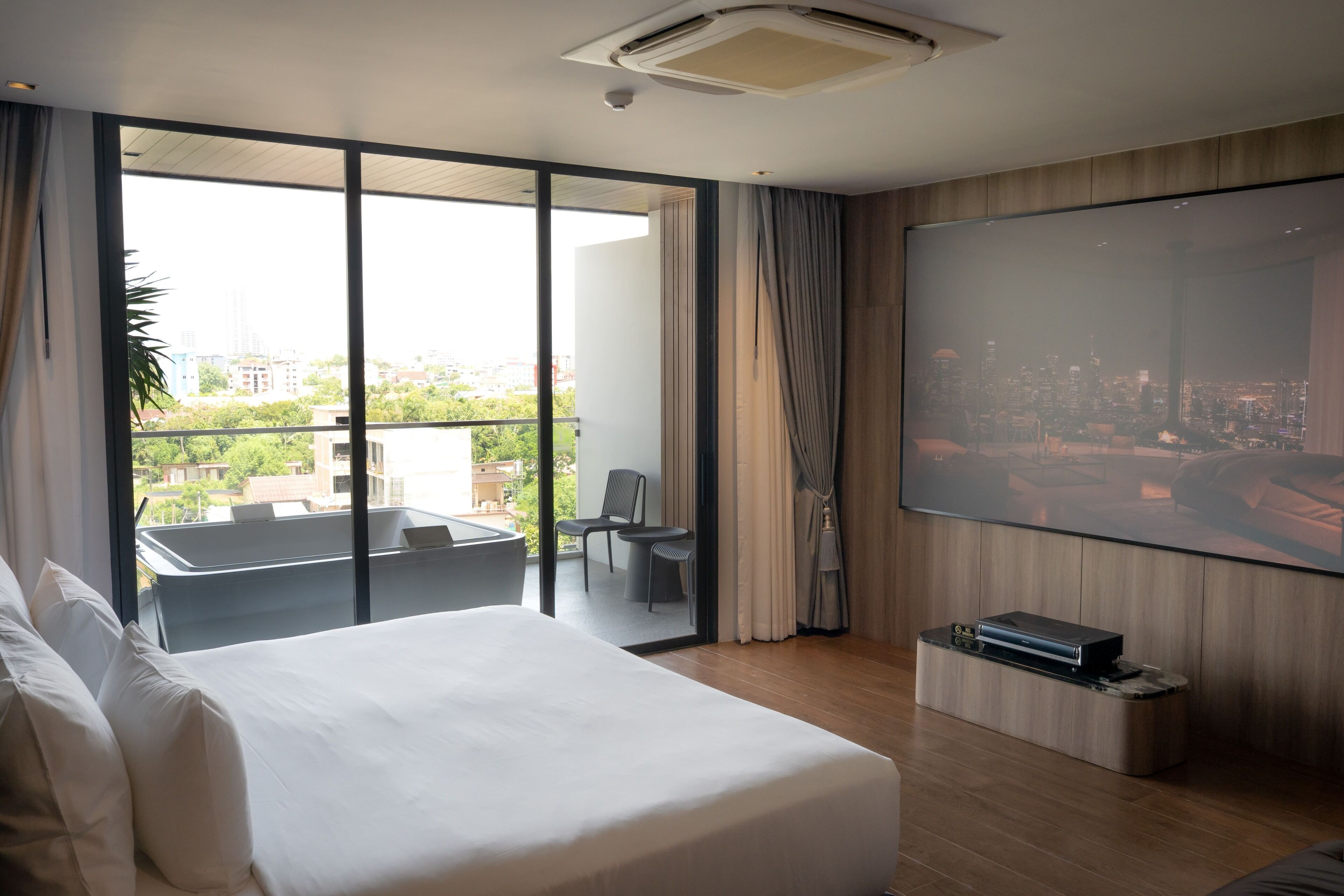 Quarto de hotel moderno com uma cama grande, varanda com vista para a cidade, televisão de tela plana e um pequeno espaço de estar.