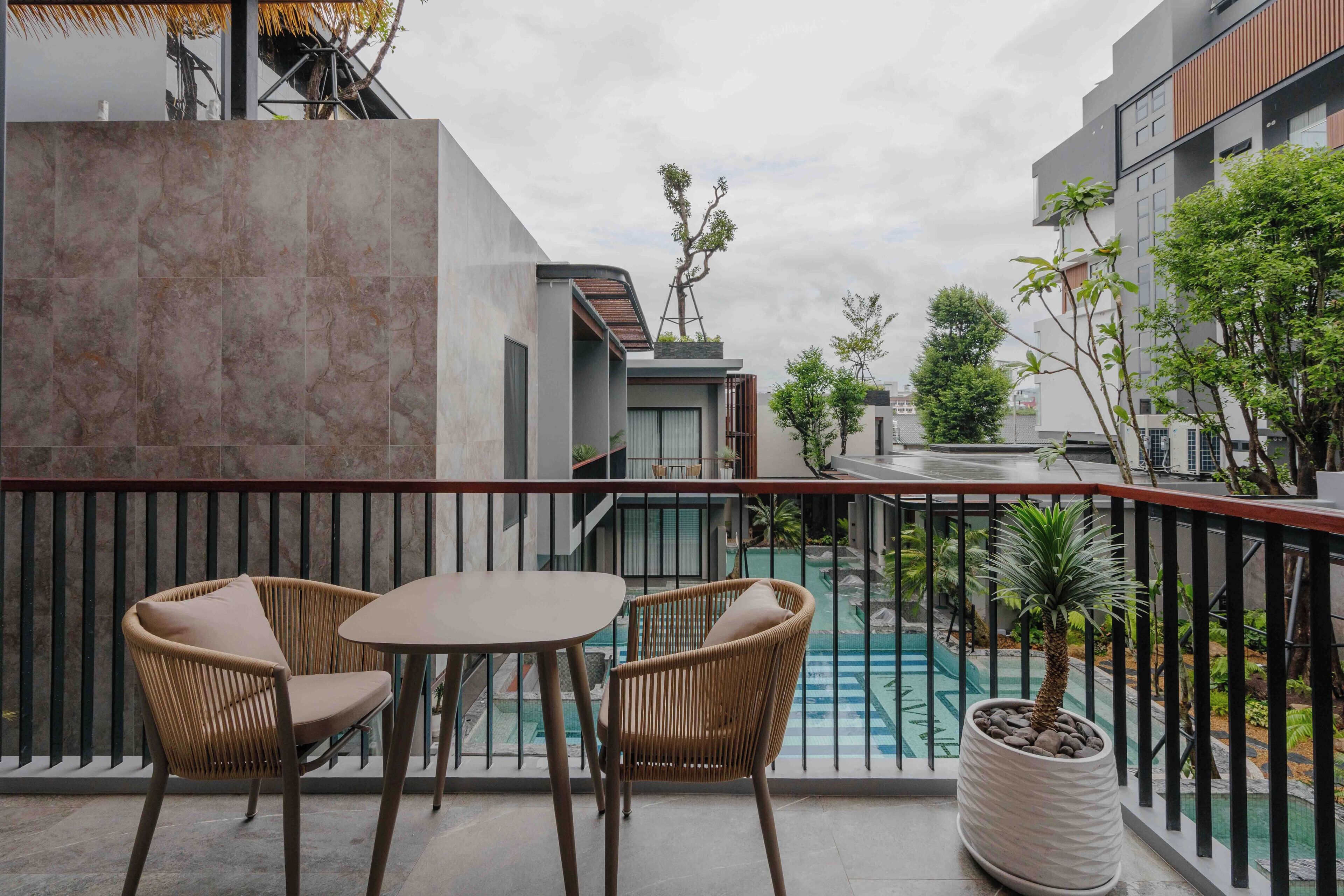 A balcony with two wicker chairs and a table, overlooking a swimming pool and surrounding greenery.