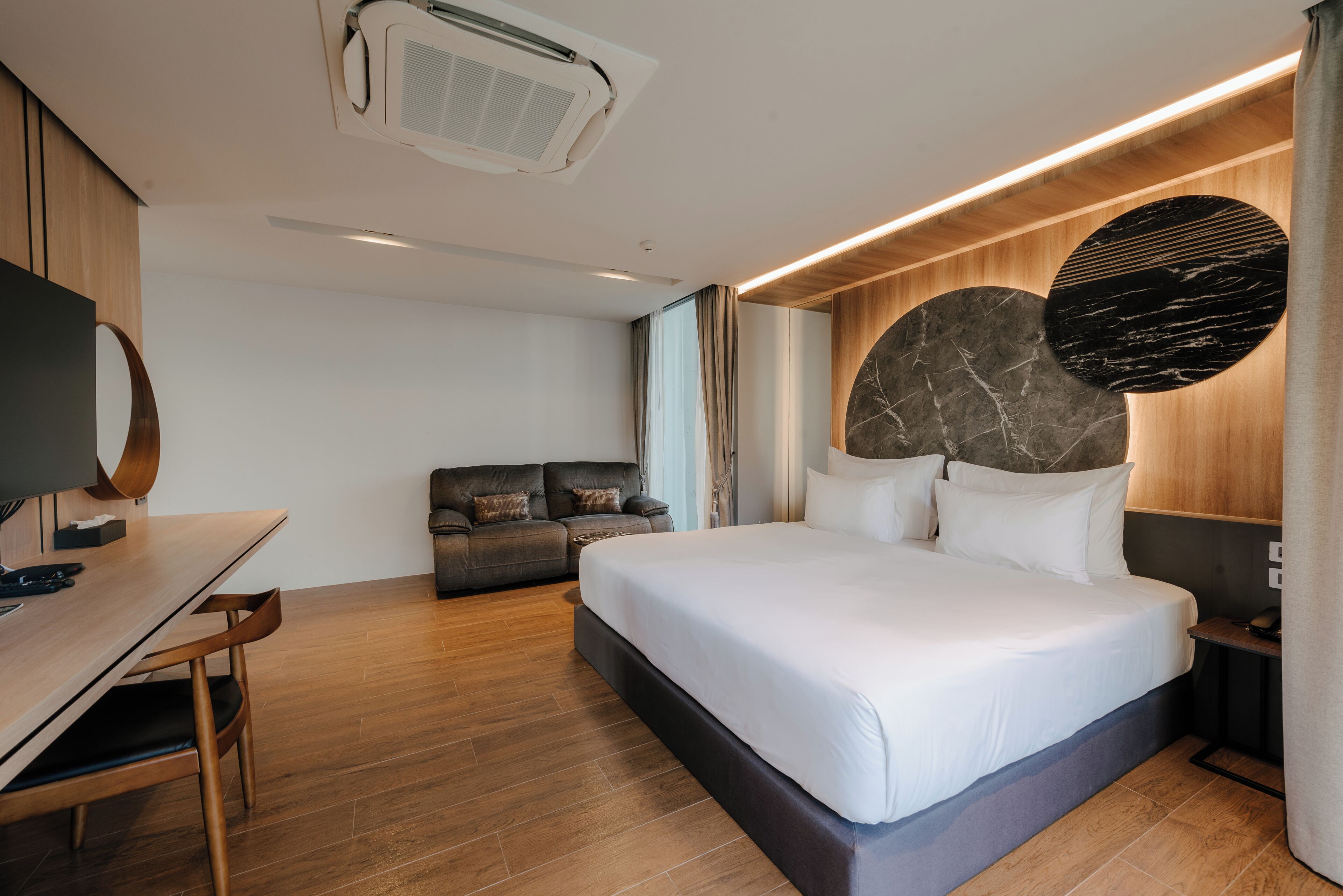 A modern hotel room with a large bed, a desk, a sofa, and a TV.