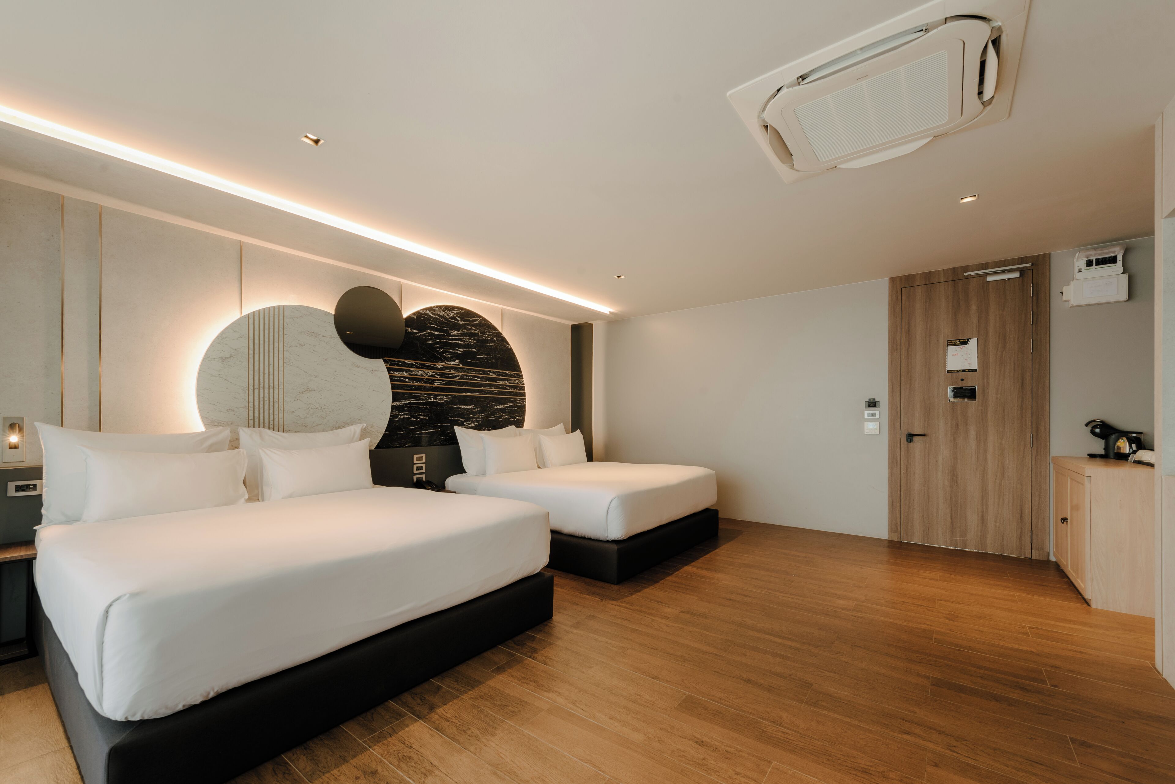 Une chambre d’hôtel moderne avec deux lits, un plancher en bois, une grande œuvre d’art abstraite accrochée au mur et un système de climatisation intégré.